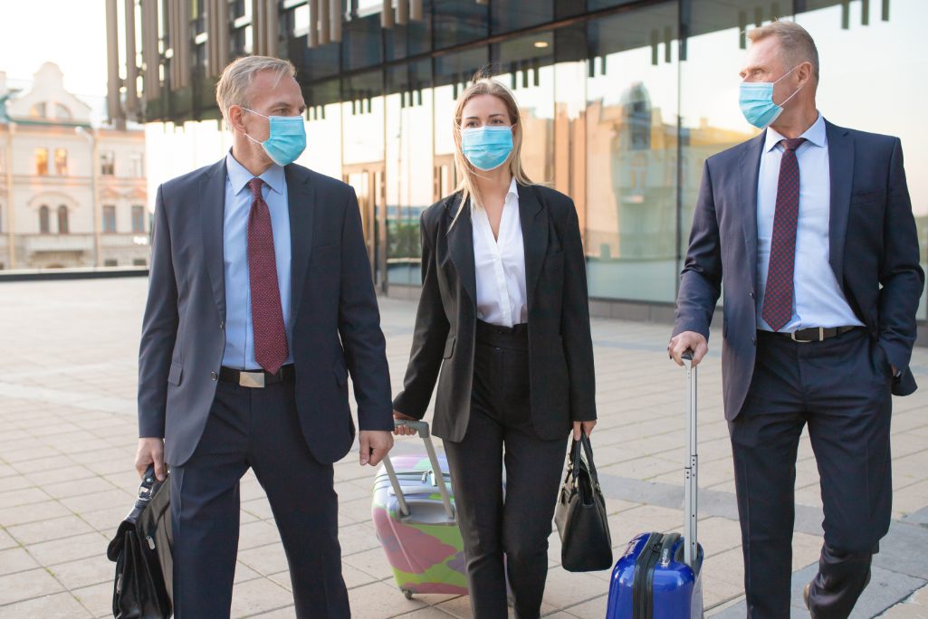 Business tourists in face masks walking outdoors Adobe