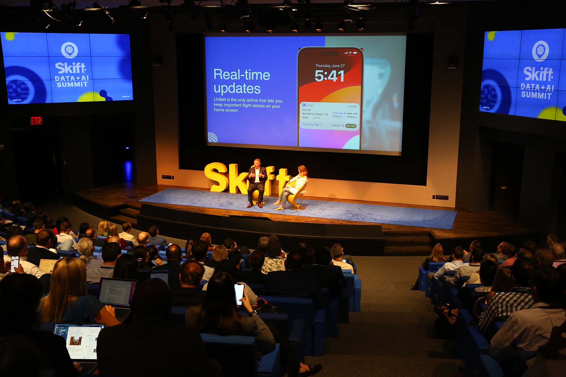 audience and stage at a conference with two people speaking on stage