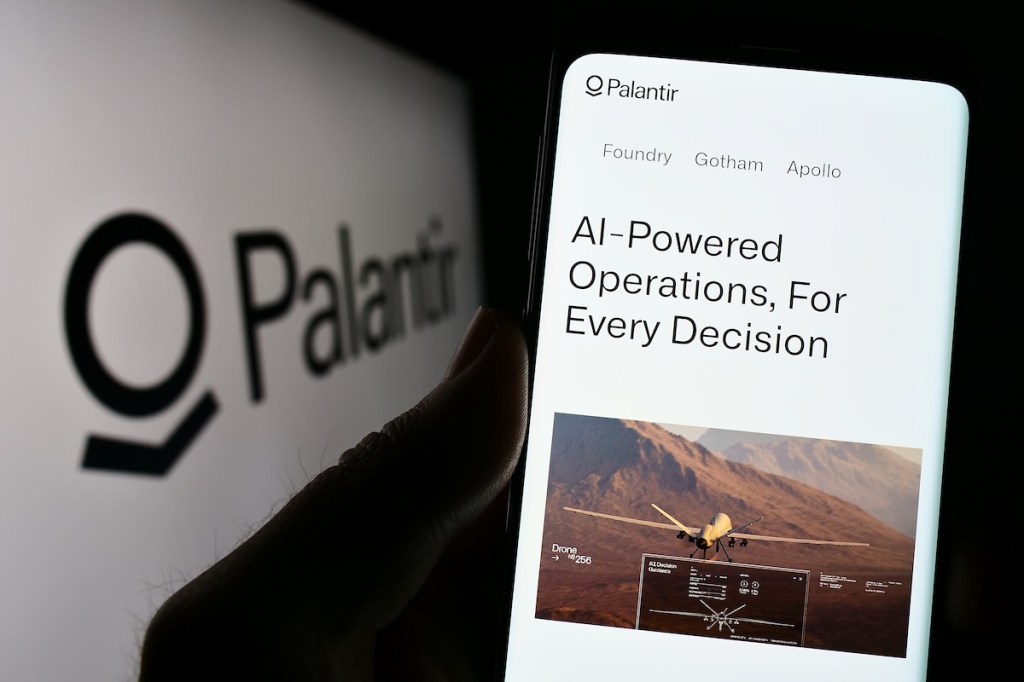 A person holding a smartphone with Palantir branding.