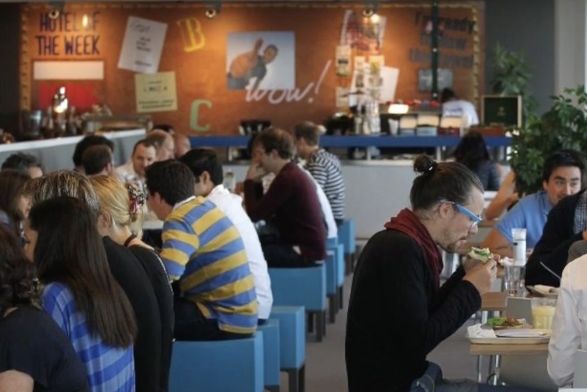 Employees at Booking.com setting at long tables and eating in a cafeteria.