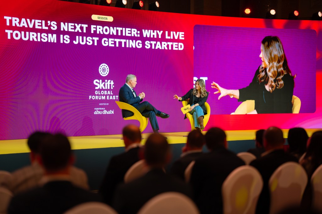 Two people sitting, talking on a stage.