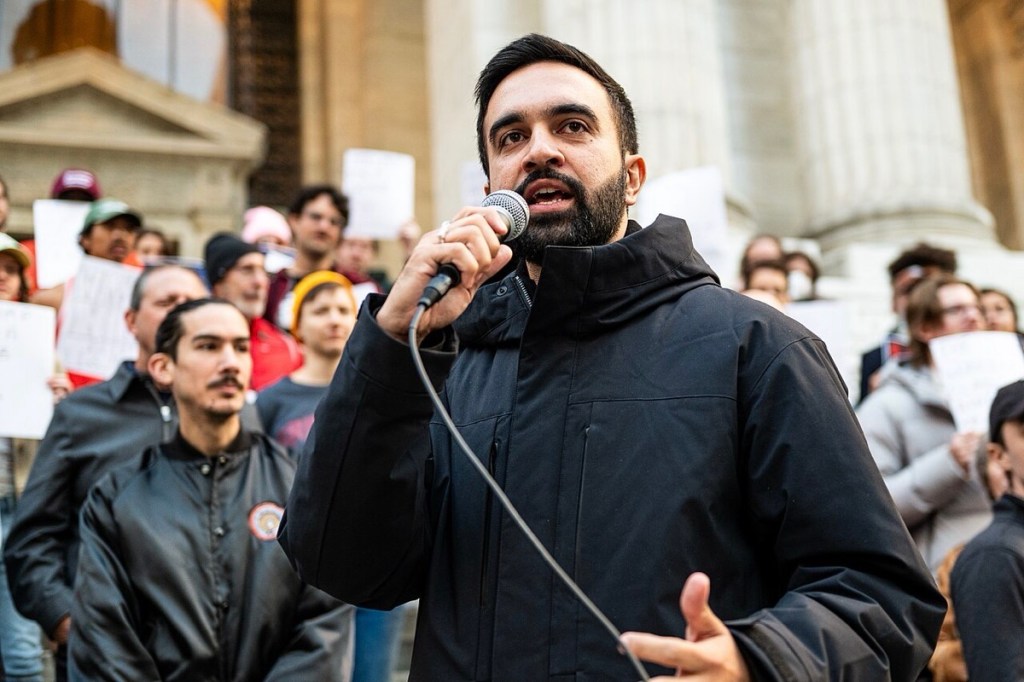 A man speaking on a microphone with people lined up behind him.