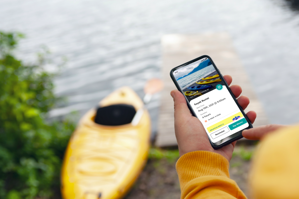 A hand holding a smart phone showing kayak rental booking details.