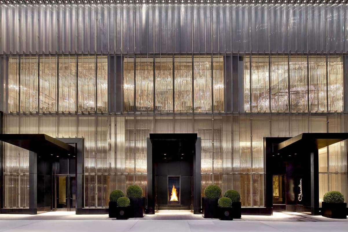 Image of the front of a Baccarat Hotel in New York City with a lot of glittering jewel tones and the view of a fireplace through a doorway on a bright sunny day