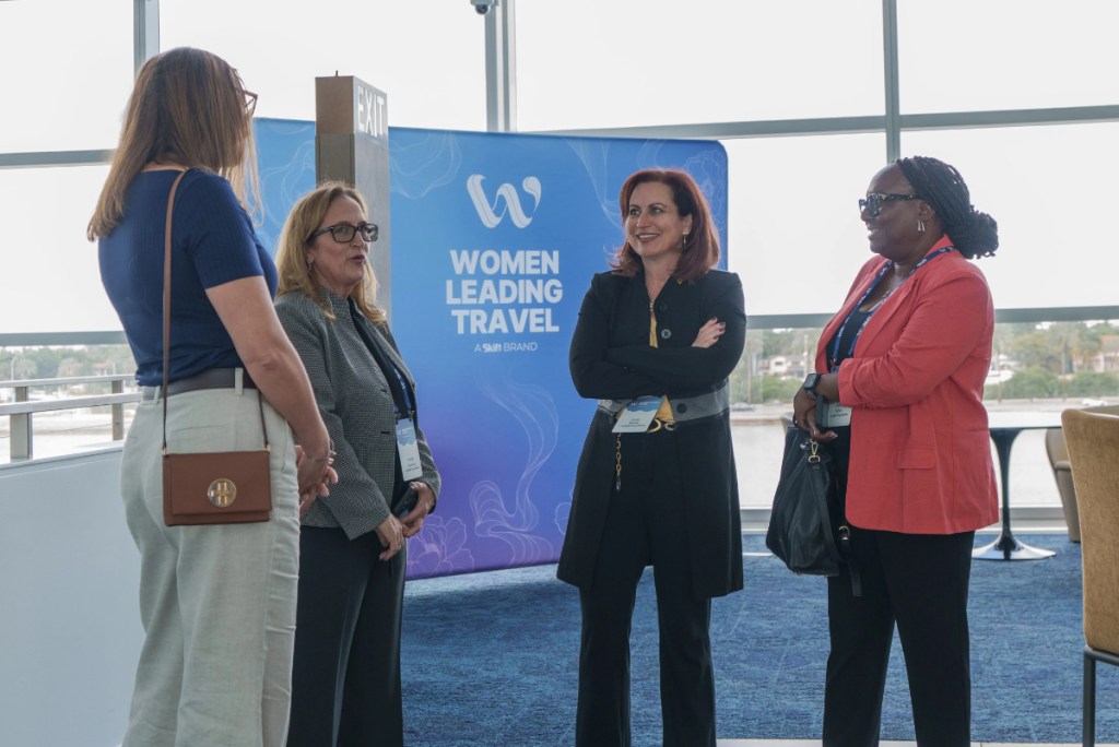 Four women standing chatting with a sign behind them saying "Women Leading Travel."