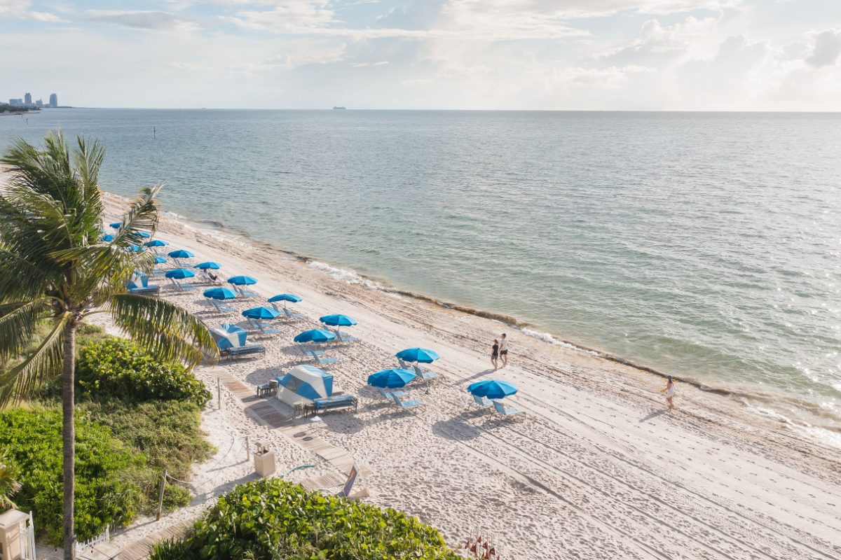 Image of the beach by the water at Key Biscayne at the Ritz-Carlton on a sunny day. There are beach umbrellas on the sand.