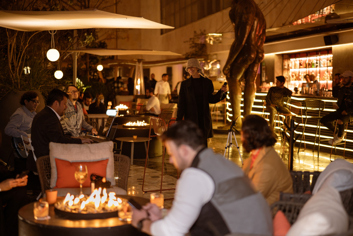 Images of a bunch of Mexican city locals hanging out at a bar with very distinctive furniture, statues, lots of lights, and a fire pit.