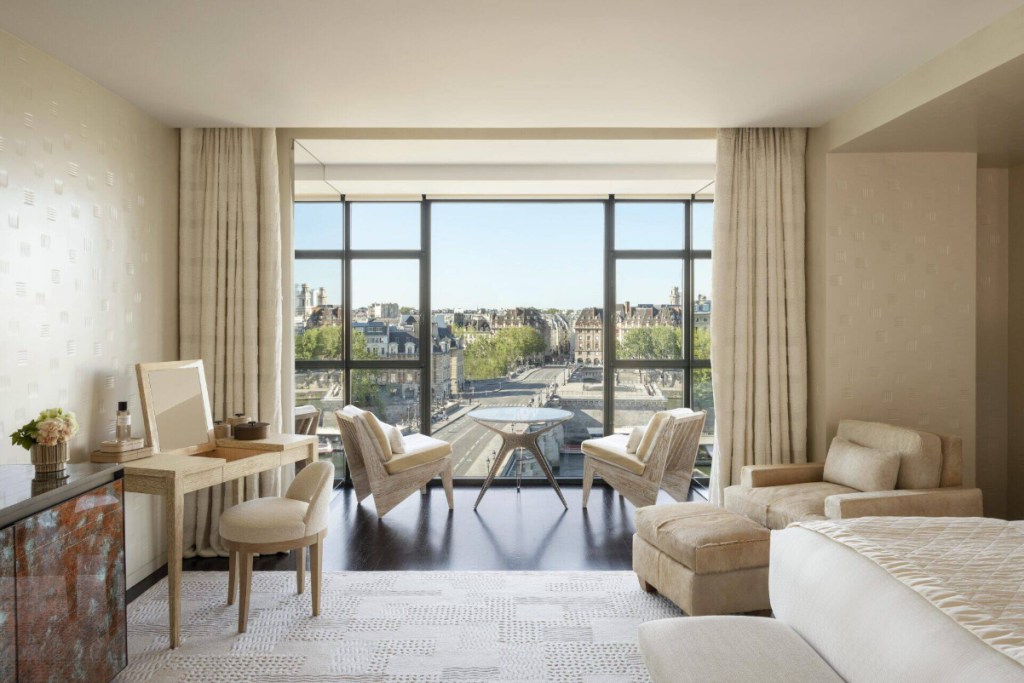 View from inside a luxury suite at a luxury hotel in Paris called Cheval Blanc Paris on a bright, sunny day. Looking out, big windows with the latest in luxury furniture.