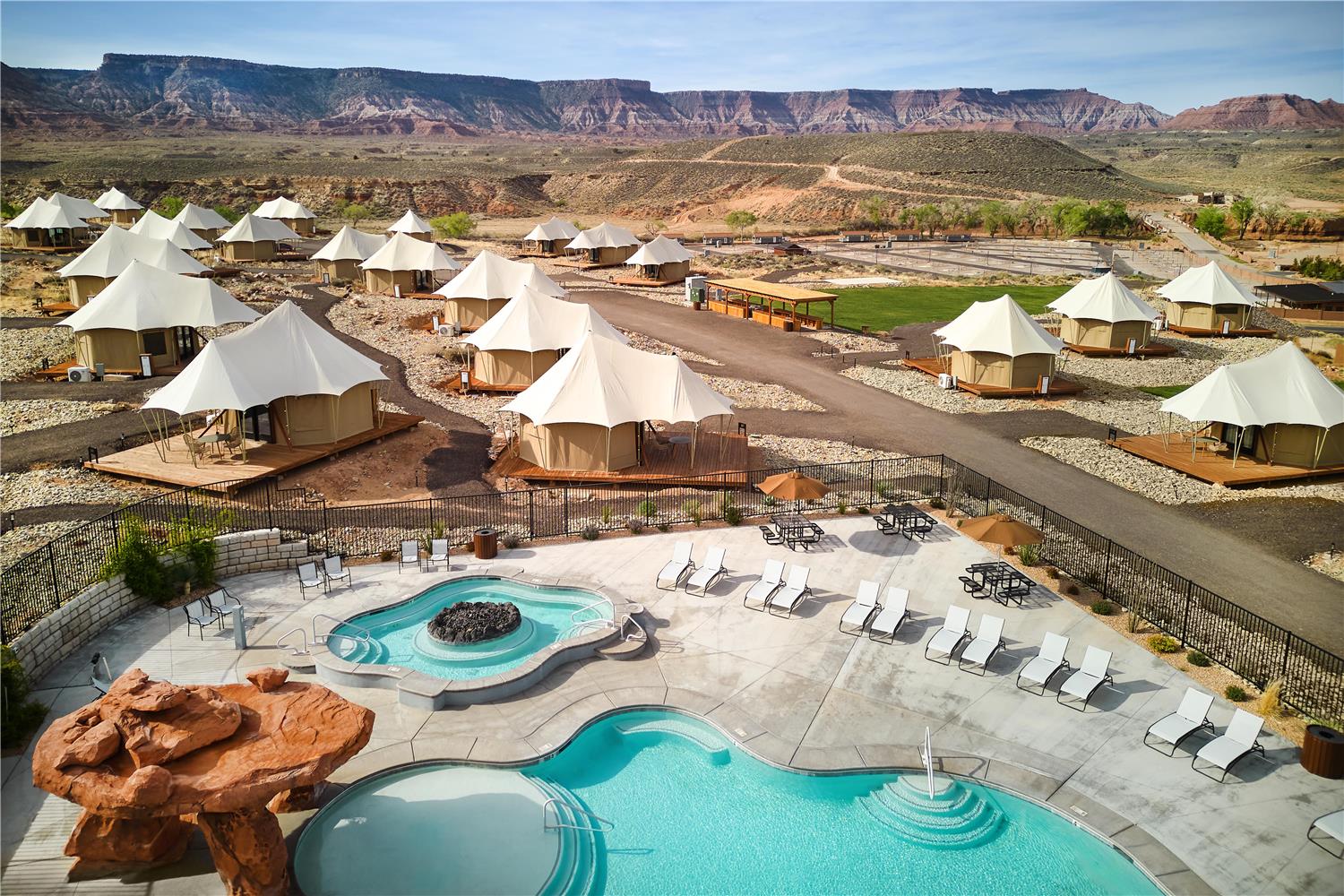 This is an image of a glamping or upscale camping resort called Zion Wildflower. Seen from above, the little luxury tents are scattered near a pool on a sunny day.