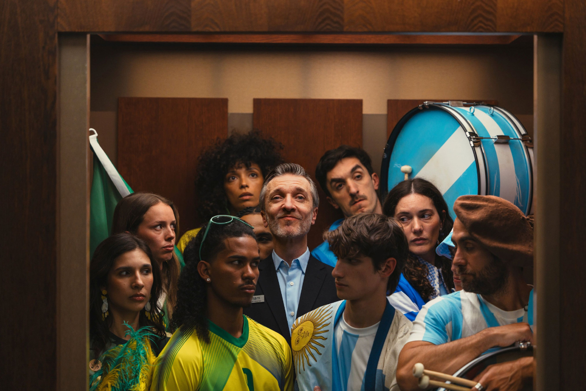 Image of football fans for Scotland's national team and Brazil's national team stuck in an elevator wearing their costumes or outfits, with a Marriott employee in the middle.